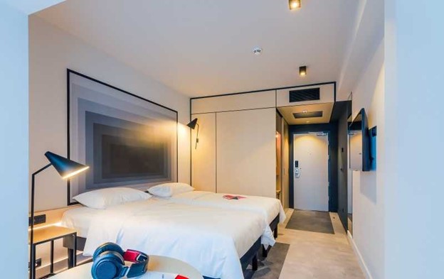Corpuri de iluminat cu LED amplasate într-o cameră de hotel, în proximitatea patului și un tablou supradimensionat